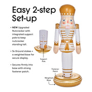 Nutcracker decoration with support pole, ground stakes, and weighted base on a white background. Copy reads: Easy 2-step Set Up. NEW upgraded nutcracker with integrated support pole to keep nutcracker standing  tall. 3x ground stakes + weighted based for secure display. Secures firmly into base with strong fastener patch.